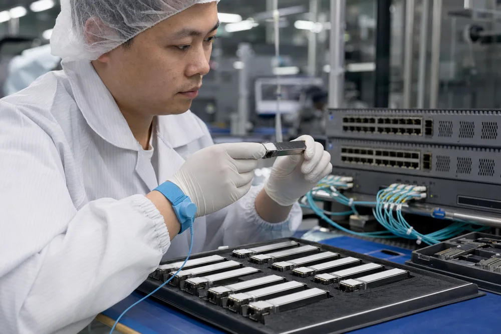 Technician inspecting labeled optical transceiver modules beside enterprise switches in a Shenzhen production facility