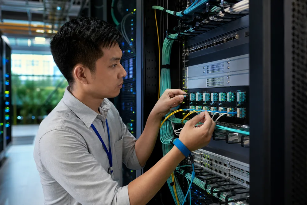 Network engineer checking labeled optical transceiver modules, LC fiber patch cords and switch ports in a Southeast Asian data center